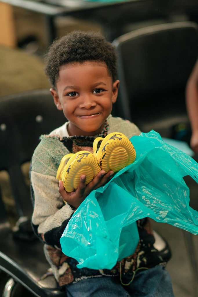 A young boy holding a pair of yellow tennis shoes.