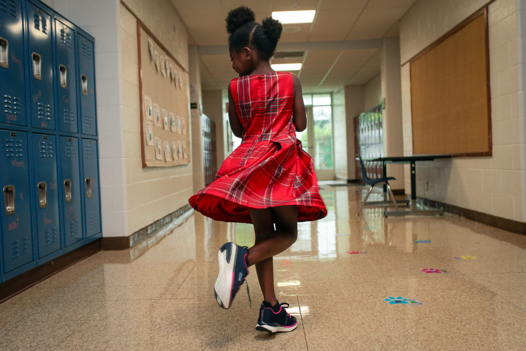 A girl in a red dress walking down a hallway.